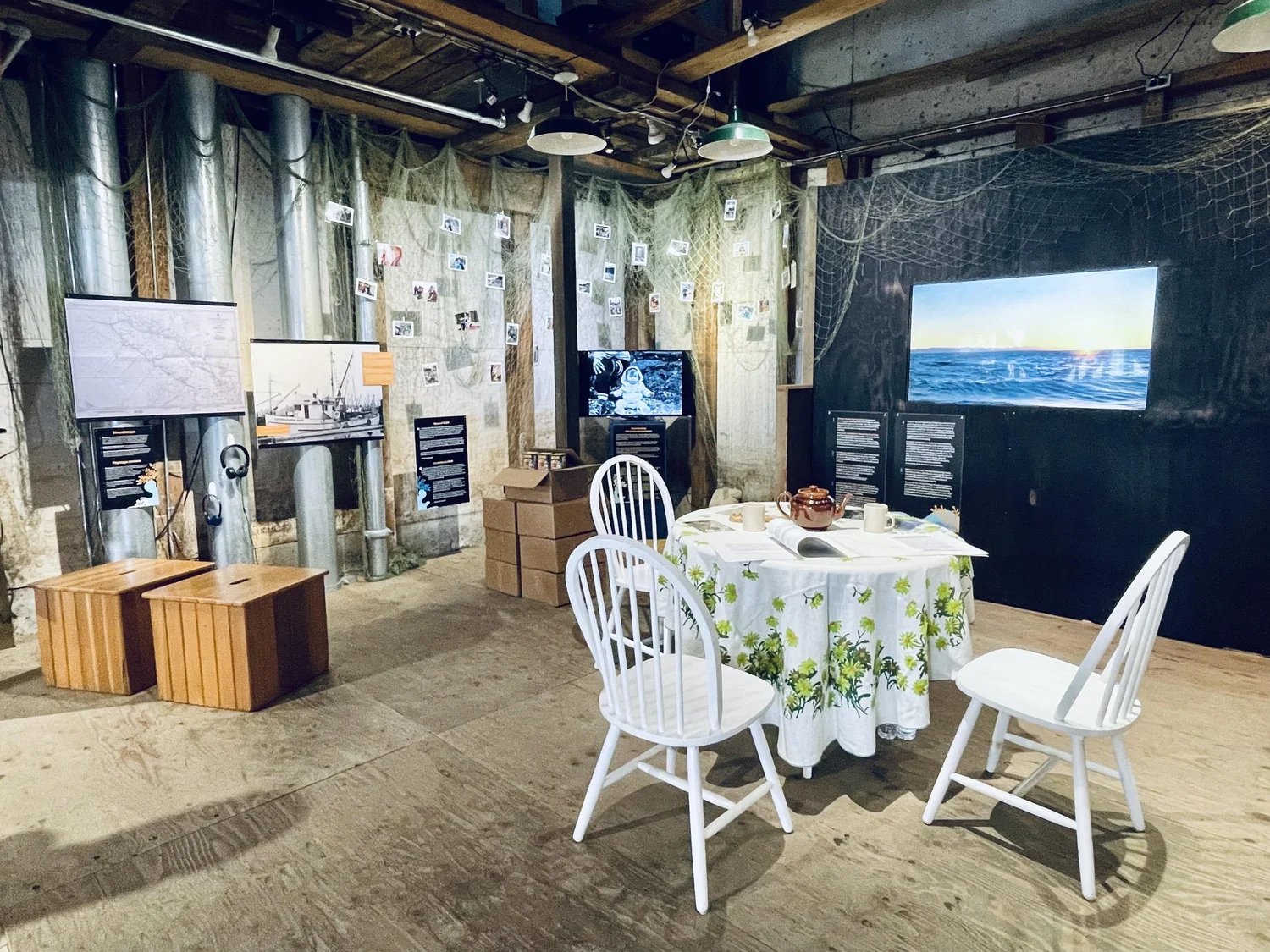 The Water We Call Home installed at the Gulf of Georgia Cannery, with photographs in fishing nets, video screens, and a table set for visitors to sit and read.